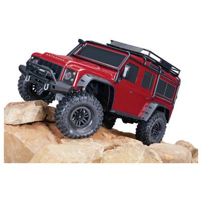 Un modèle de véhicule tout-terrain rouge avec de grandes roues est positionné sur un terrain rocailleux, mettant en valeur sa conception robuste et ses détails.