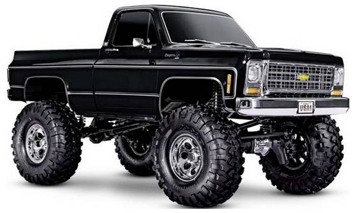 Un camion pickup vintage noir surélevé, équipé de grands pneus tout-terrain et d'une calandre chromée, stationné sur un fond blanc.