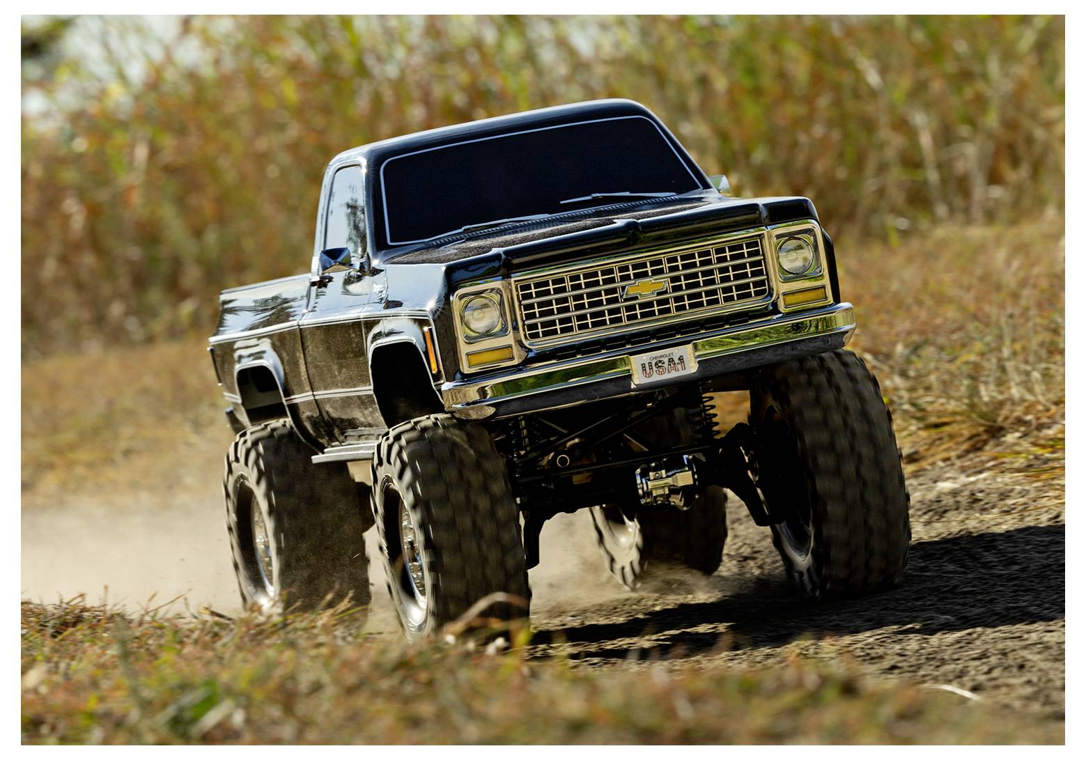 Un camion tout-terrain surélevé avec de grandes roues circule sur un chemin de terre, entouré d'herbe verte, évoquant un cadre d'aventure en plein air.