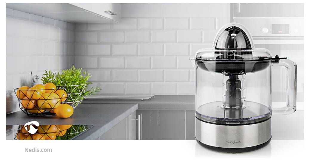 Un presse-agrumes moderne posé sur un plan de travail de cuisine avec un bol d'oranges. Carrelage blanc en crédence et accessoires en acier inoxydable en arrière-plan.