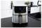 Un air fryer en acier inoxydable sur un plan de travail de cuisine avec un affichage numérique indiquant '180°C'. Des ustensiles de cuisine et des plantes sont visibles en arrière-plan.