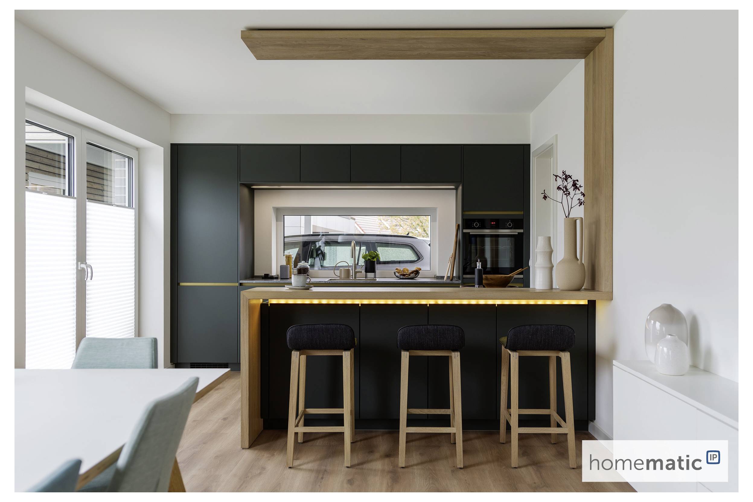Une cuisine moderne avec un îlot vert foncé, trois tabourets en bois, et une grande fenêtre donnant sur une voiture garée à l'extérieur.