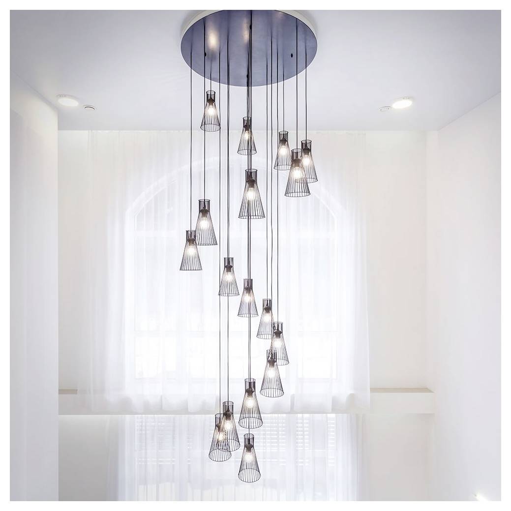 Un lustre moderne avec plusieurs suspensions lumineuses est suspendu à un plafond élevé, diffusant une lueur douce dans une pièce lumineuse aux rideaux transparents.