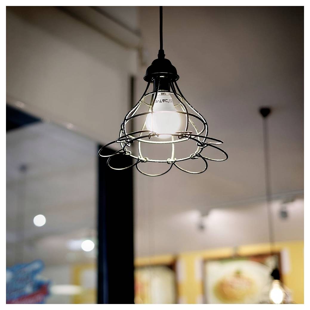 Une ampoule suspendue avec un cadre métallique décoratif est allumée dans un intérieur moderne, créant une atmosphère chaleureuse et accueillante.