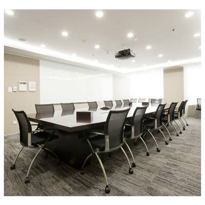Une salle de conférence moderne avec une longue table, plusieurs chaises, un projecteur au plafond et un éclairage lumineux, suggérant un espace dédié aux réunions.
