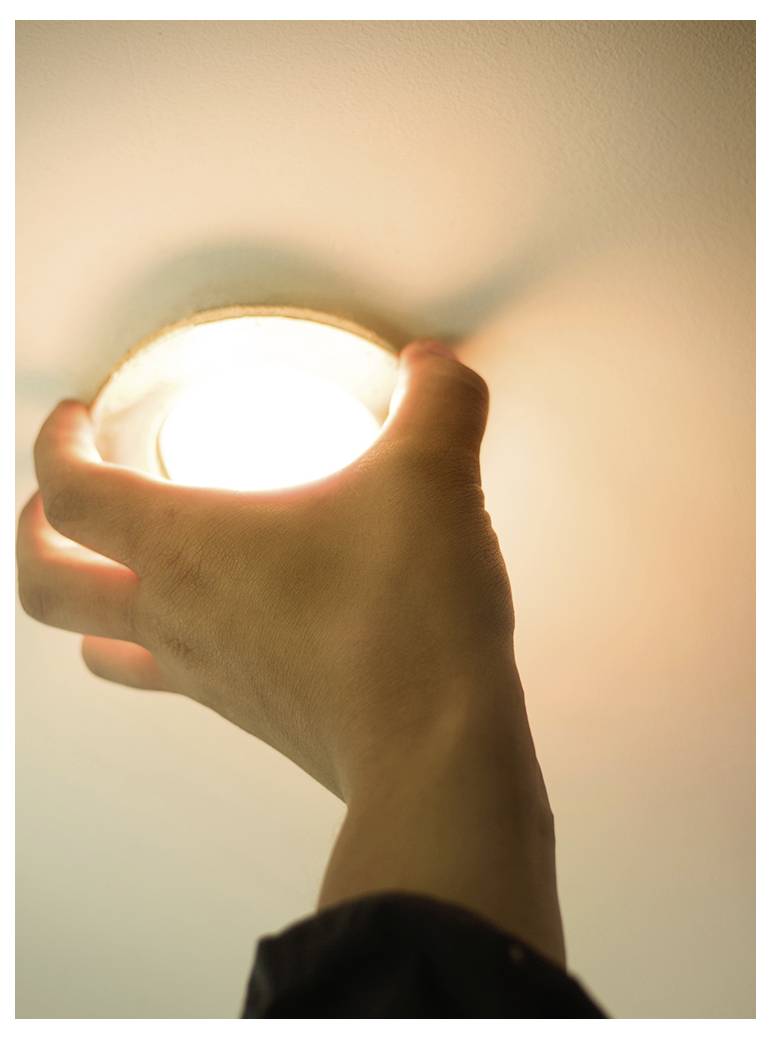 Une main est en train d'installer ou de retirer une ampoule allumée dans un luminaire de plafond, suggérant une maintenance ou un remplacement de l'appareil.