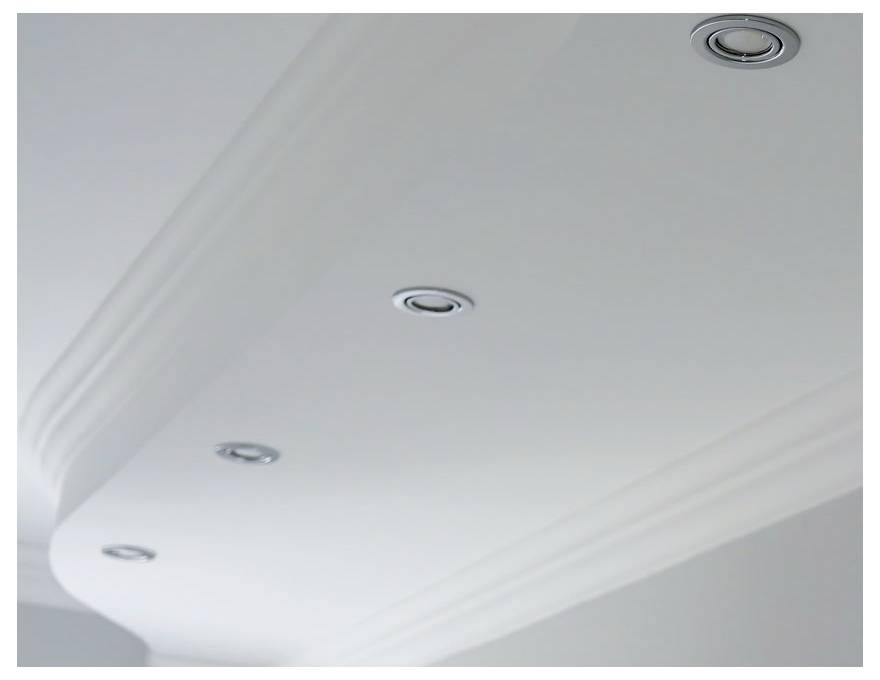 Un plafond blanc avec quatre luminaires encastrés circulaires espacés uniformément.