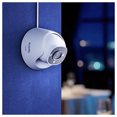 Une caméra de sécurité fixée sur un mur bleu, braquée sur une pièce faiblement éclairée avec des lumières floues en arrière-plan.