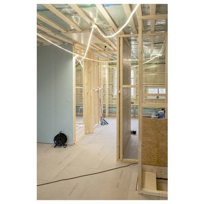 Une pièce en cours de construction avec une charpente en bois apparente et de l'isolation, des câbles électriques sont visibles ; une fenêtre est visible en arrière-plan.