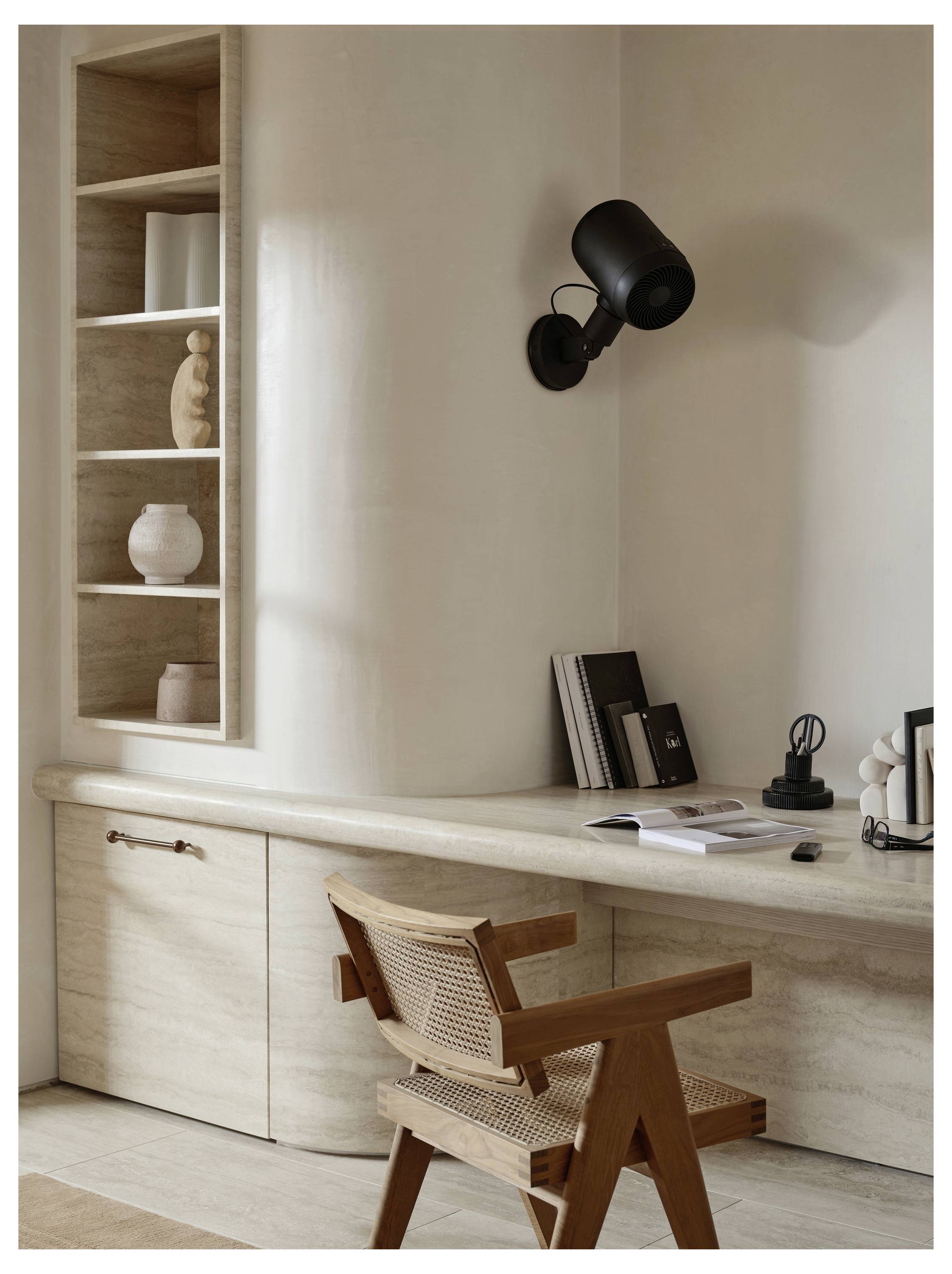 Un coin de bureau à domicile minimaliste avec un bureau en bois et une chaise, une lampe noire murale, et des étagères supportant des objets décoratifs et des livres.
