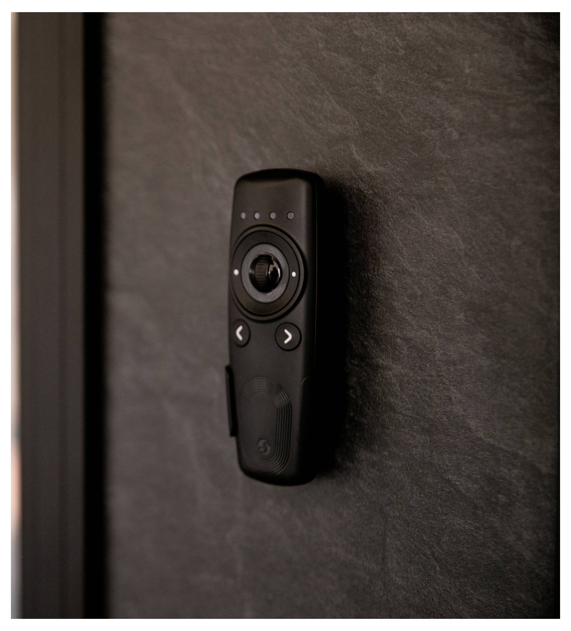Une télécommande noire montée sur un mur texturé sombre, dotée de boutons et d'un pavé de contrôle circulaire central.