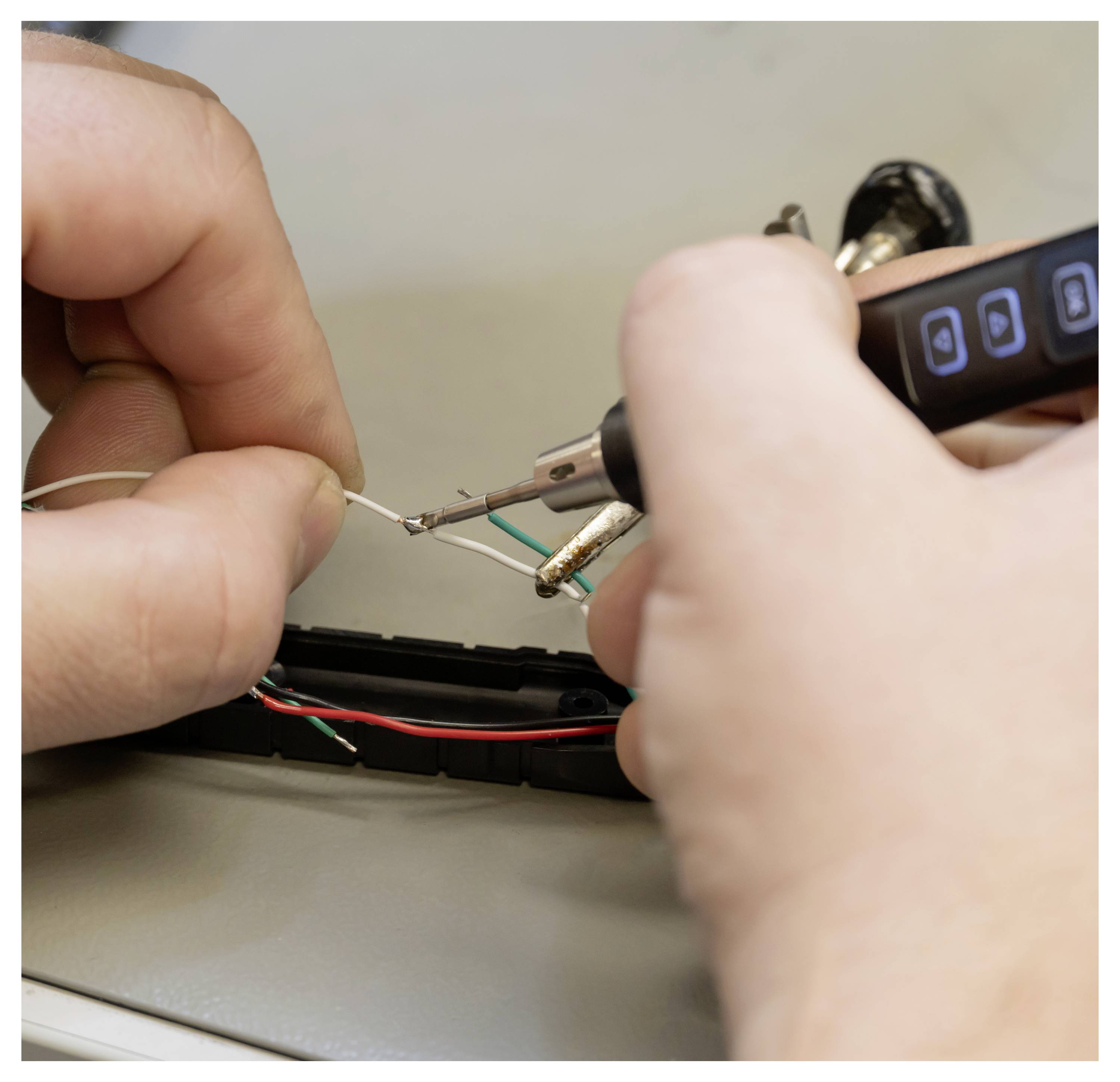 Les mains utilisant un fer à souder pour joindre de fins fils dans un petit appareil électronique lors d'une réparation.
