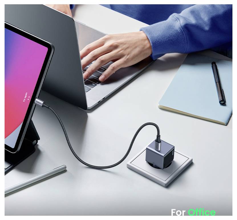 Une personne tape sur un ordinateur portable connecté à une tablette par un câble, avec un carnet de notes et un stylo à proximité.