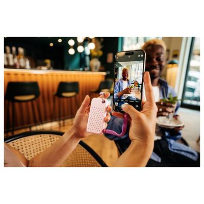 Une personne photographiant un homme souriant tenant un verre et un dessert dans un café, avec l'écran du téléphone affichant l'aperçu en direct.