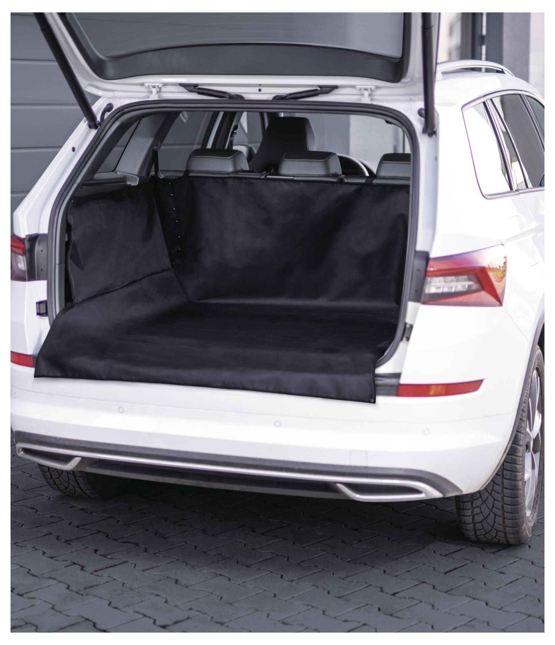 Une voiture blanche avec un coffre ouvert doublé d'une housse de protection noire, garée sur une surface carrelée dans un cadre urbain.
