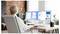 Une femme est assise à un bureau avec deux moniteurs affichant des documents et des applications, dans un bureau à domicile moderne bien éclairé.