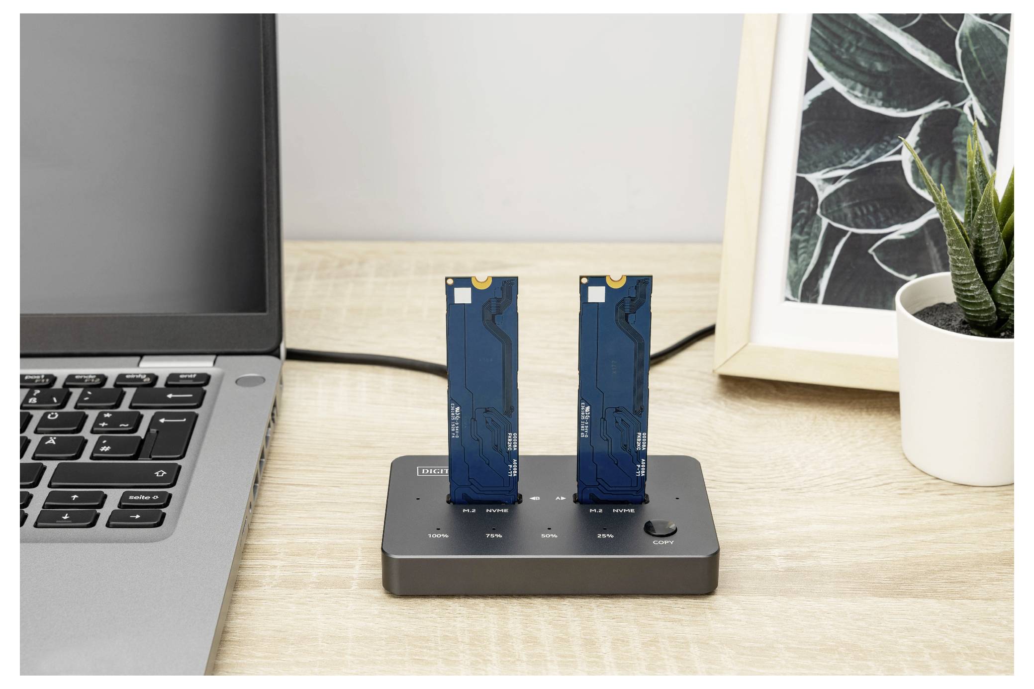 « Deux SSD M.2 bleus insérés dans un socle d'accueil noir à côté d'un ordinateur portable et d'une peinture abstraite de feuille encadrée sur un bureau en bois. »