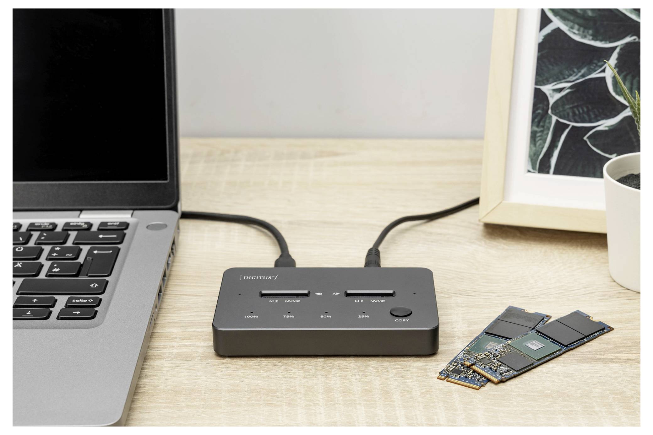 Un concentrateur USB avec plusieurs ports est connecté à un ordinateur portable sur un bureau en bois. Deux lecteurs M.2 sont placés à côté du concentrateur.