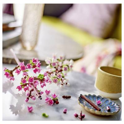 Un gros plan de petites décorations de fleurs artificielles roses et vertes sur une surface en marbre, à côté d'une tasse beige et d'une assiette décorée.