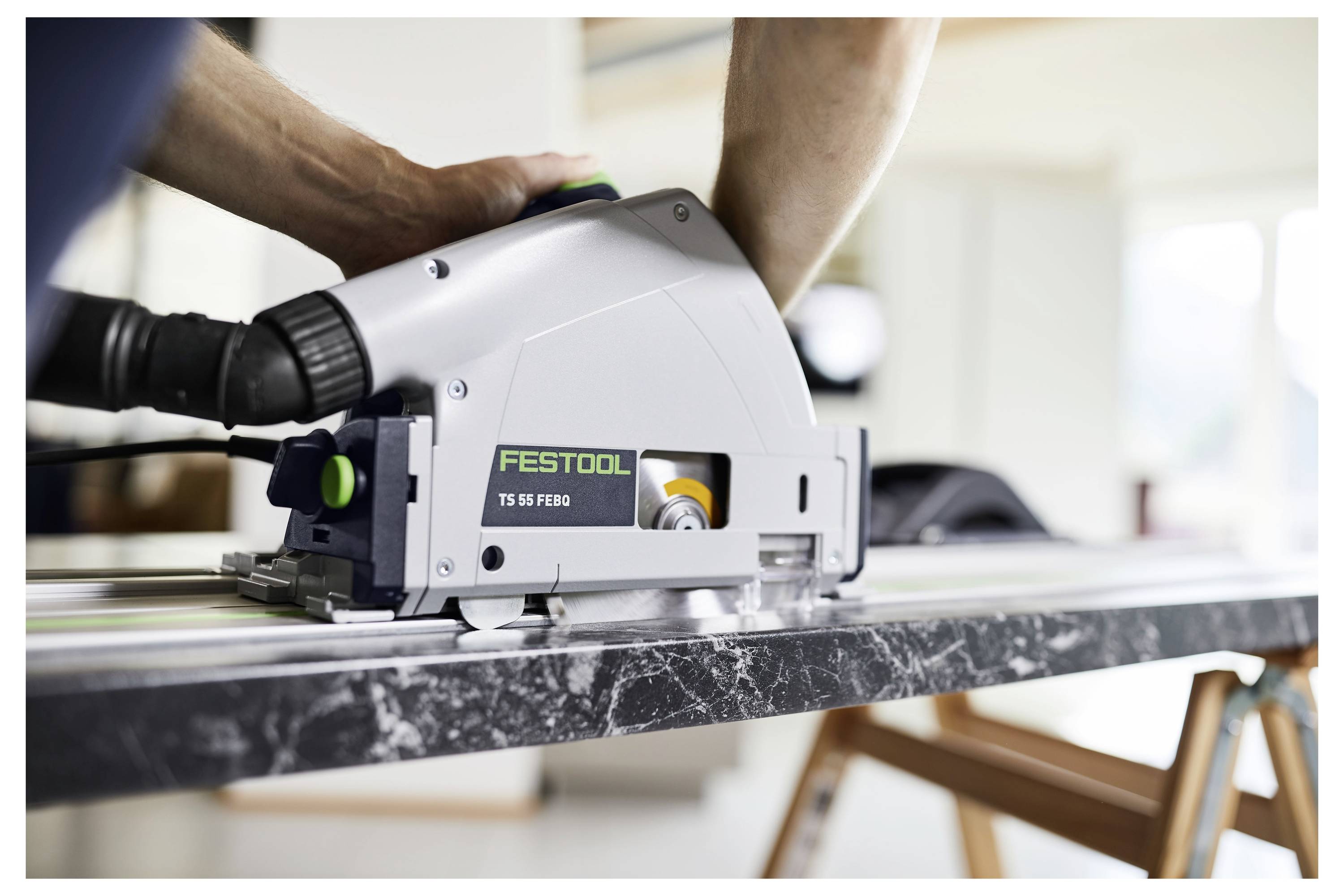 Une personne utilisant une scie circulaire Festool TS 55 FEBQ pour couper un morceau de marbre foncé sur un établi.