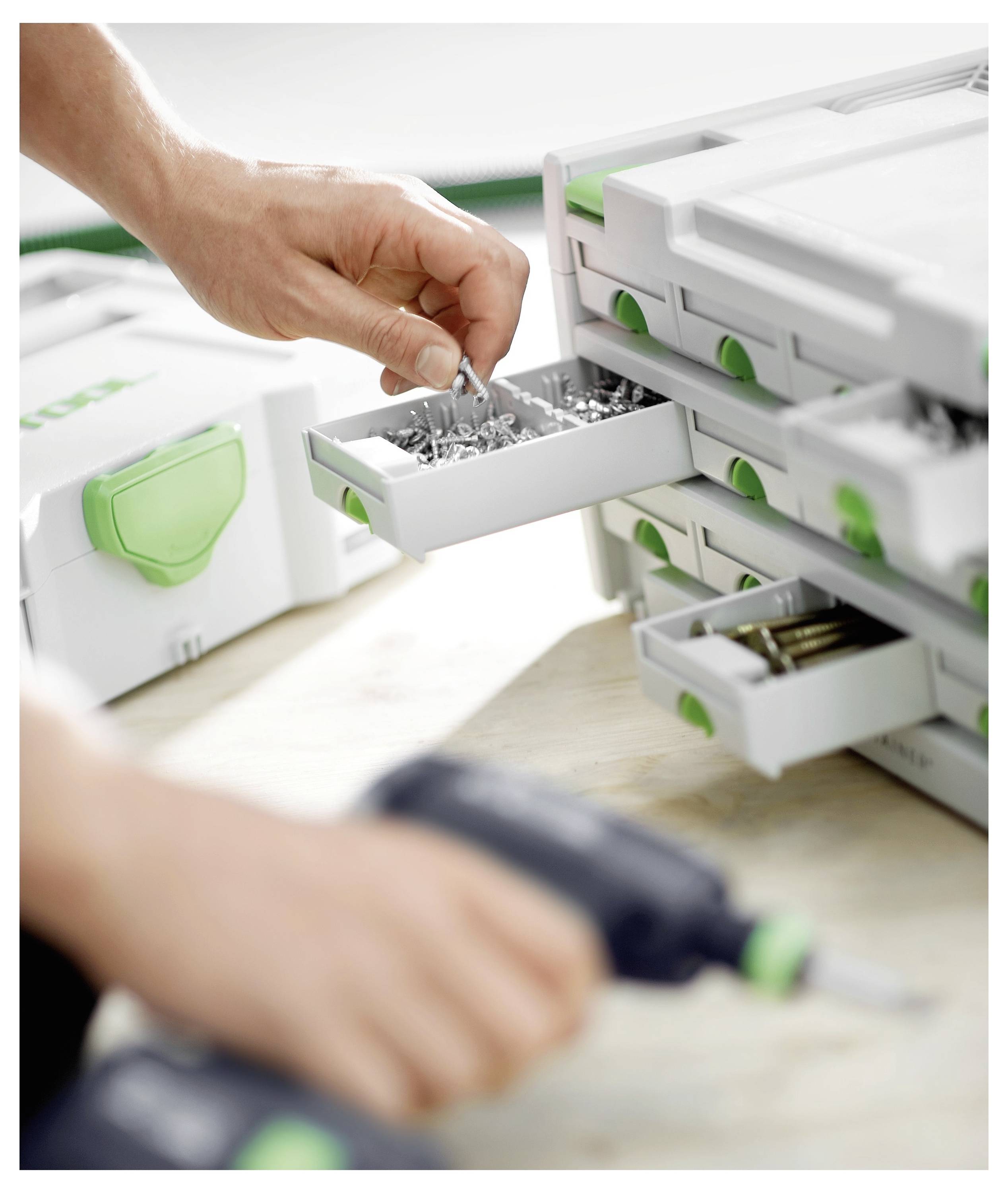 Une personne organise des vis en métal dans une boîte de rangement pour outils blanche et verte, en utilisant un tournevis électrique.