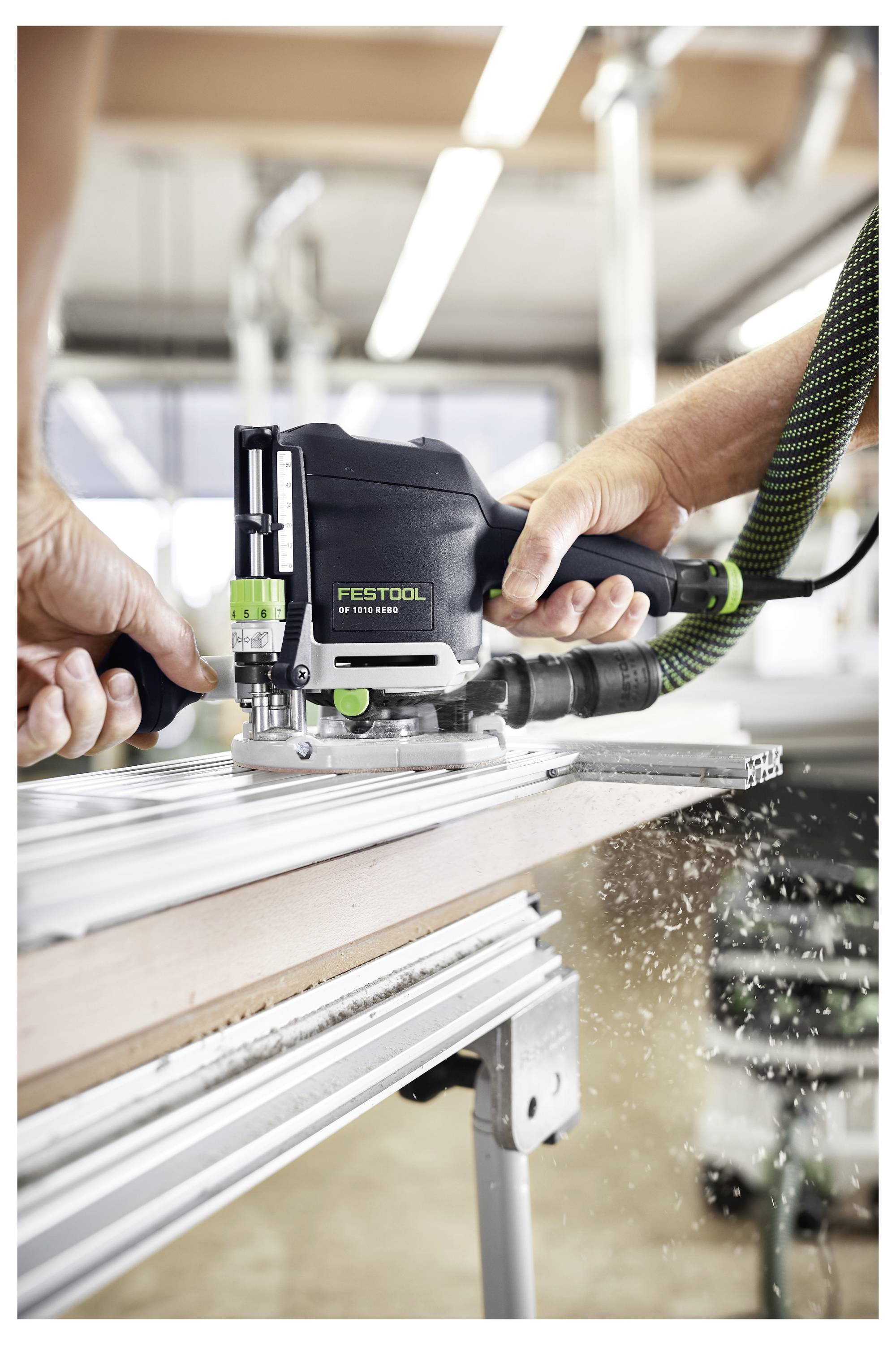 Une personne utilise une défonceuse Festool pour découper une planche en bois. L'outil est positionné sur un guide métallique pour la précision, dans un atelier.