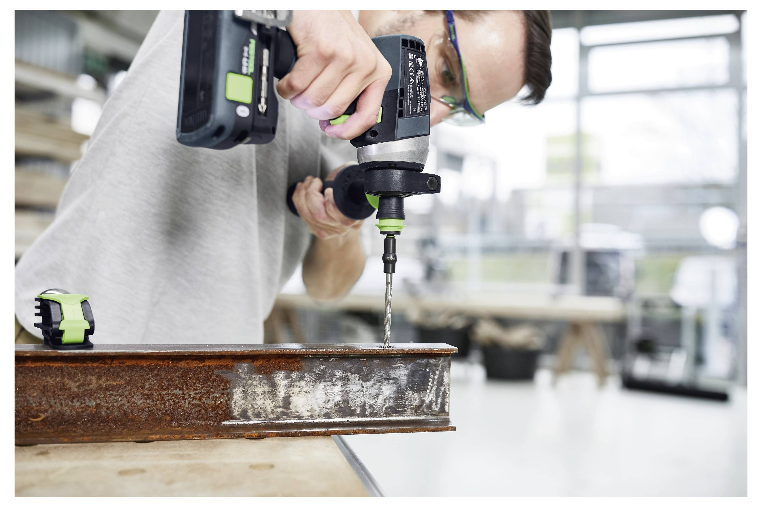 Un gros plan d'une perceuse électrique avec un foret attaché, prête à être utilisée. L'arrière-plan est flou, suggérant un environnement d'atelier.