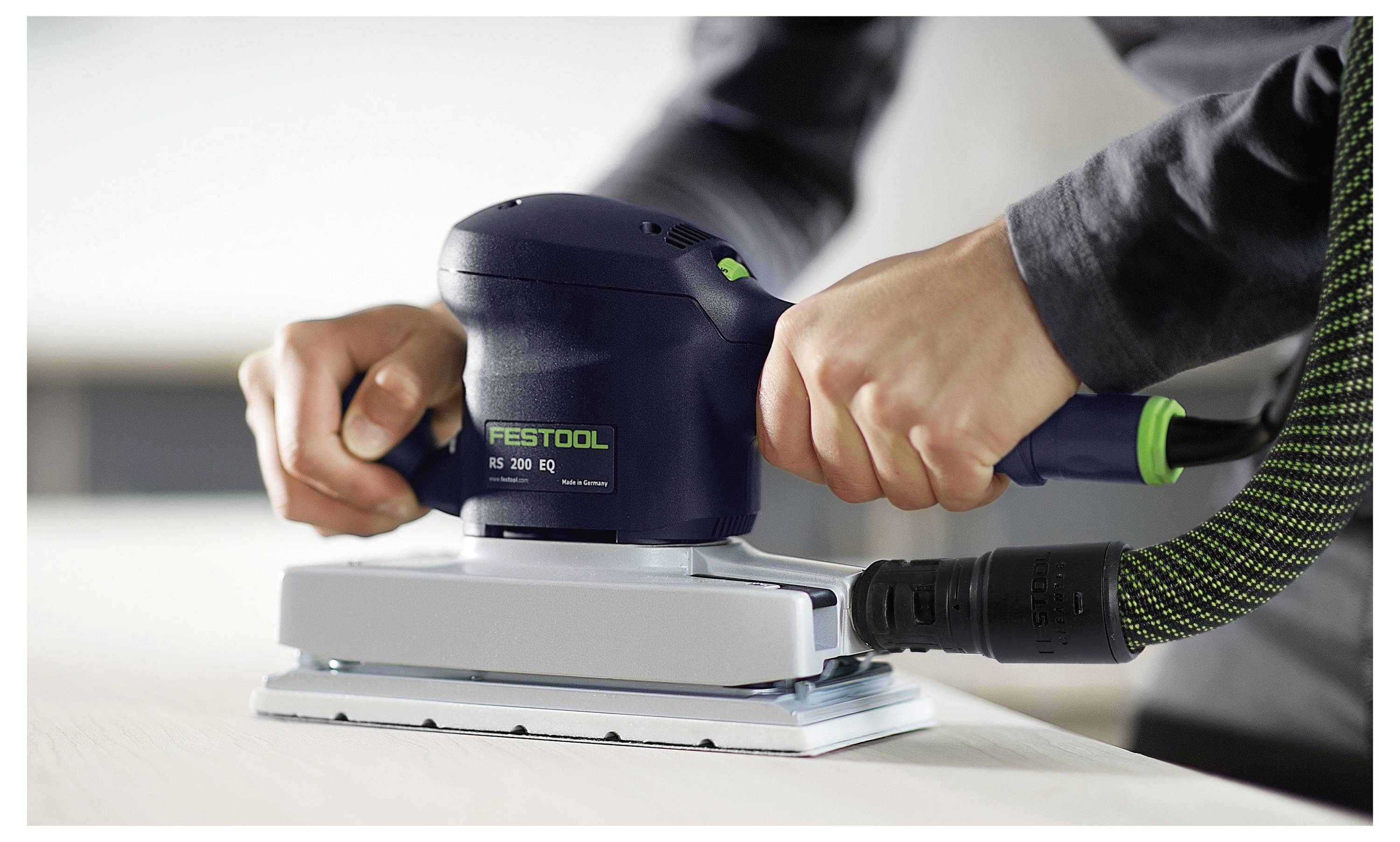 Des mains utilisant une ponceuse électrique Festool sur une surface en bois plane, la lissant. La ponceuse est reliée à un tuyau d'extraction de poussière.