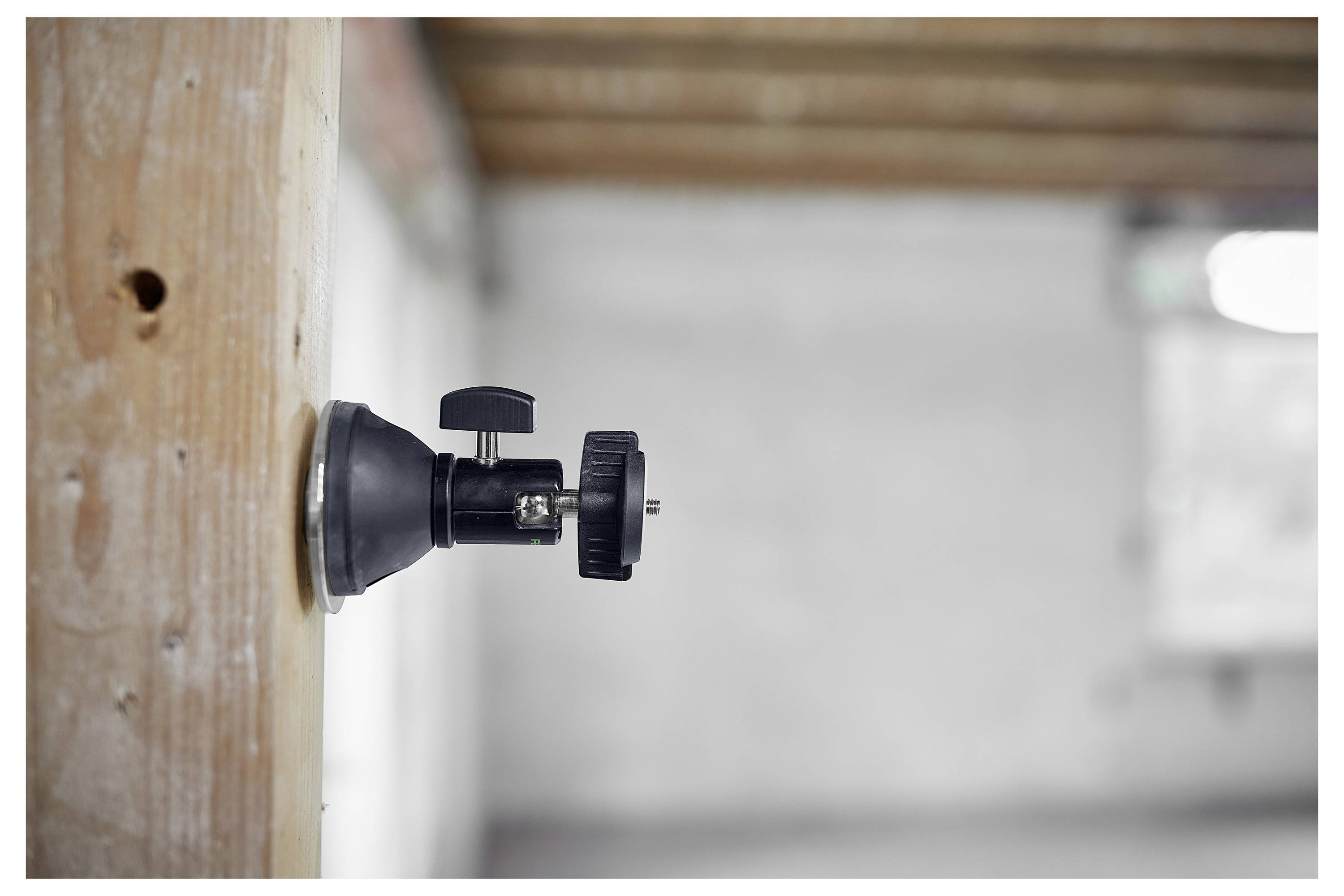 « Vue latérale d'un support de caméra fixé à une surface en bois dans une pièce inachevée, avec un arrière-plan flou de murs et de plafond. »