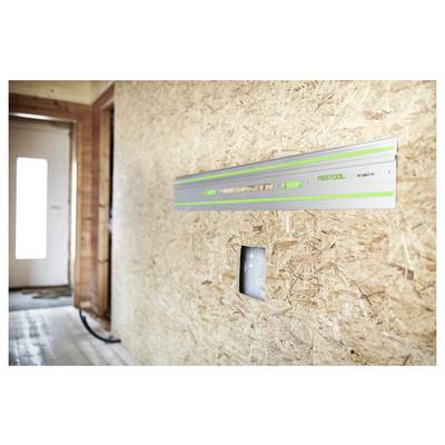 Une règle en métal avec des accents verts est montée sur un mur en bois à l'intérieur d'une pièce. La lumière naturelle entre par une porte en arrière-plan.