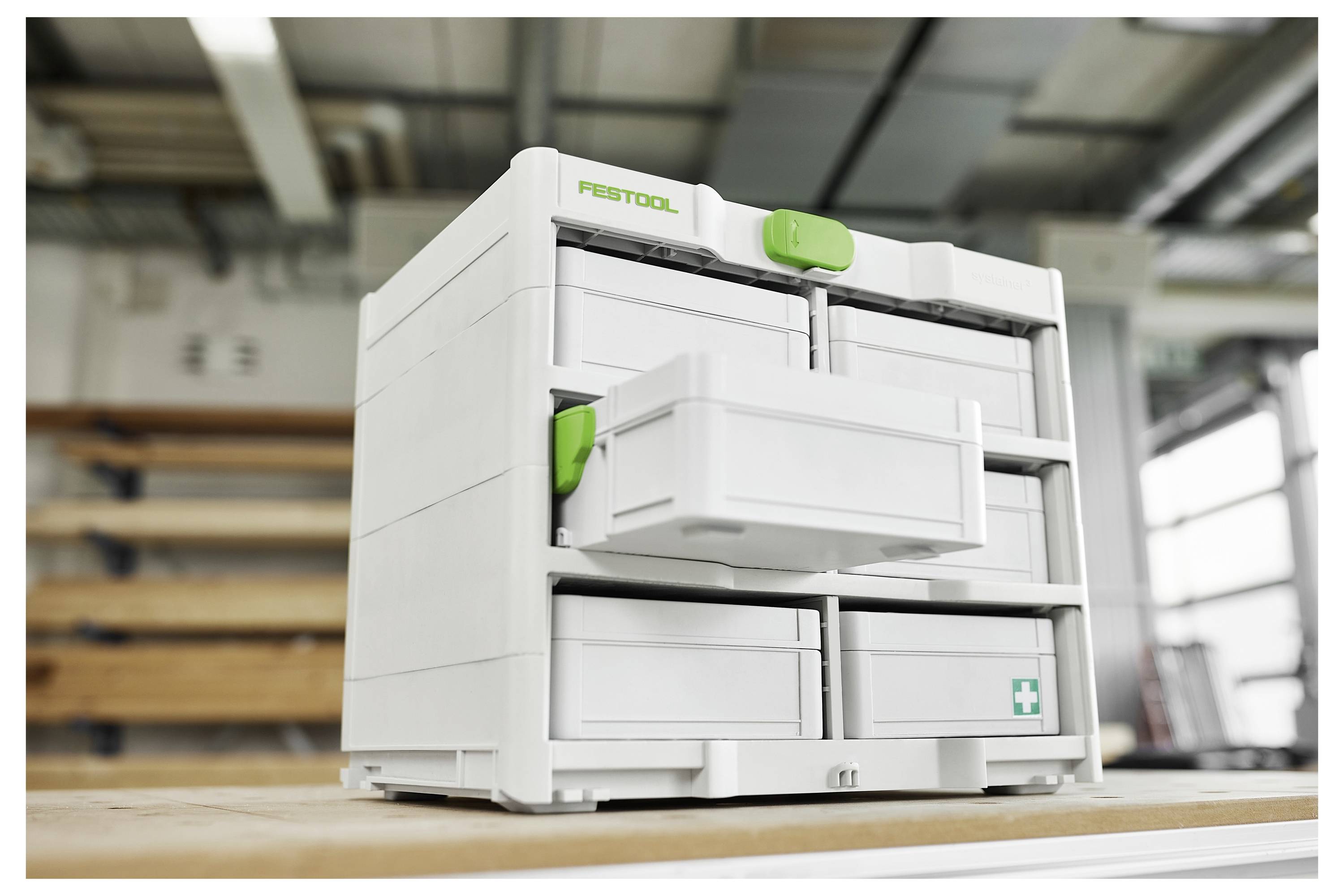 Une boîte à outils Festool blanche avec plusieurs tiroirs et des poignées vertes, présentée sur un établi dans un environnement d'atelier.