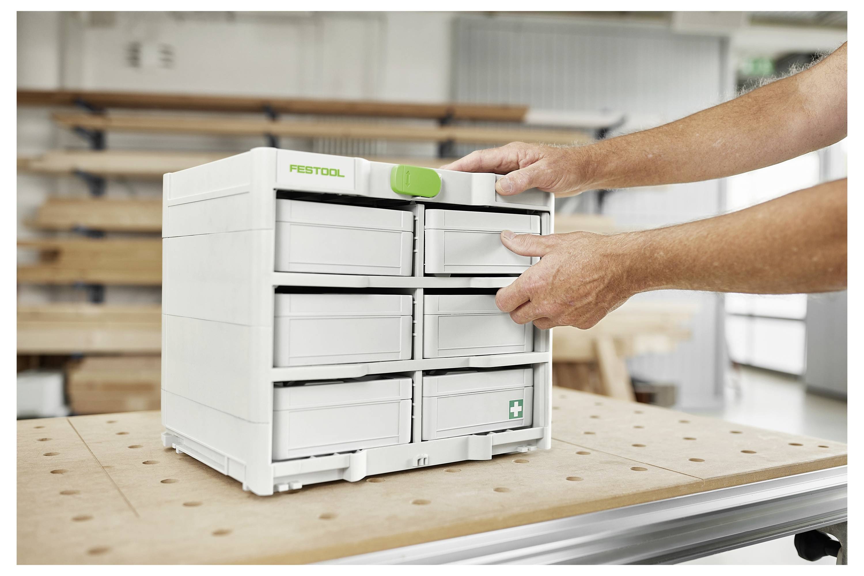 Une personne ouvre un tiroir de rangement Systainer sys-dock dans un atelier, avec des outils de menuiserie et des matériaux visibles en arrière-plan.