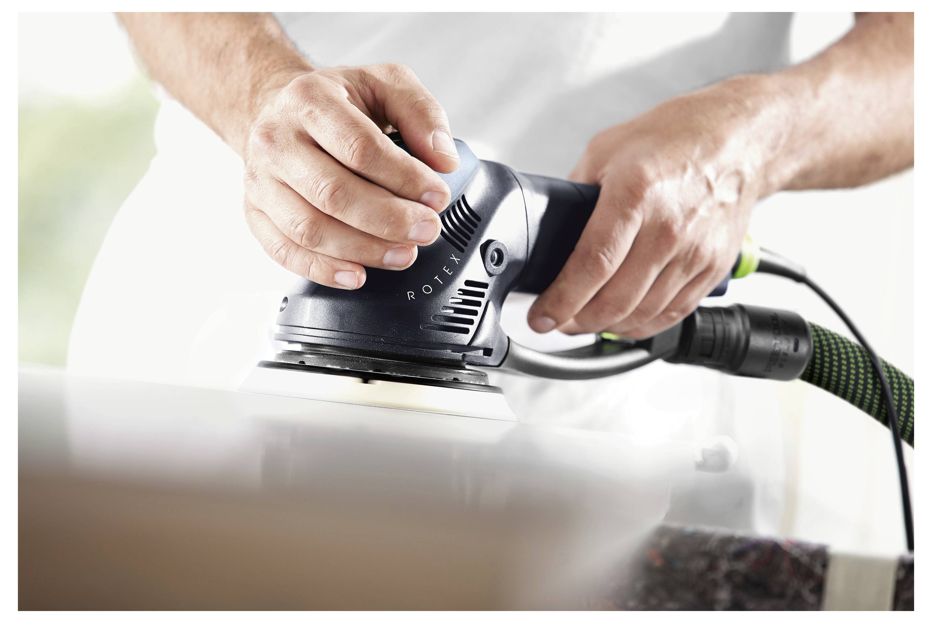 Une personne utilisant une ponceuse électrique pour lisser une surface en bois, se concentrant sur les mains tenant l'outil, mettant en avant un travail de menuiserie en cours.