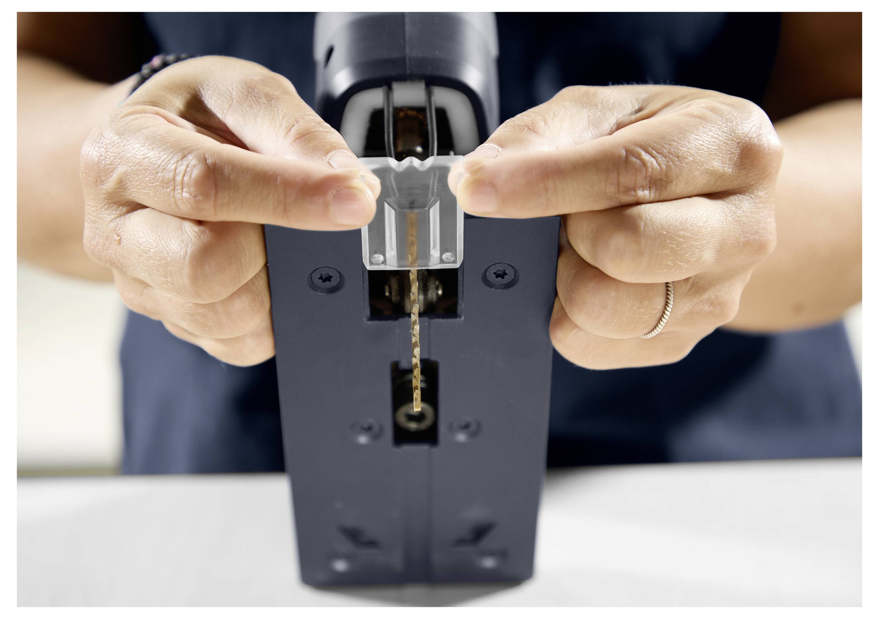 Une personne portant des lunettes de sécurité et des gants utilise un outil électrique Festool, se concentrant intensément sur la tâche.