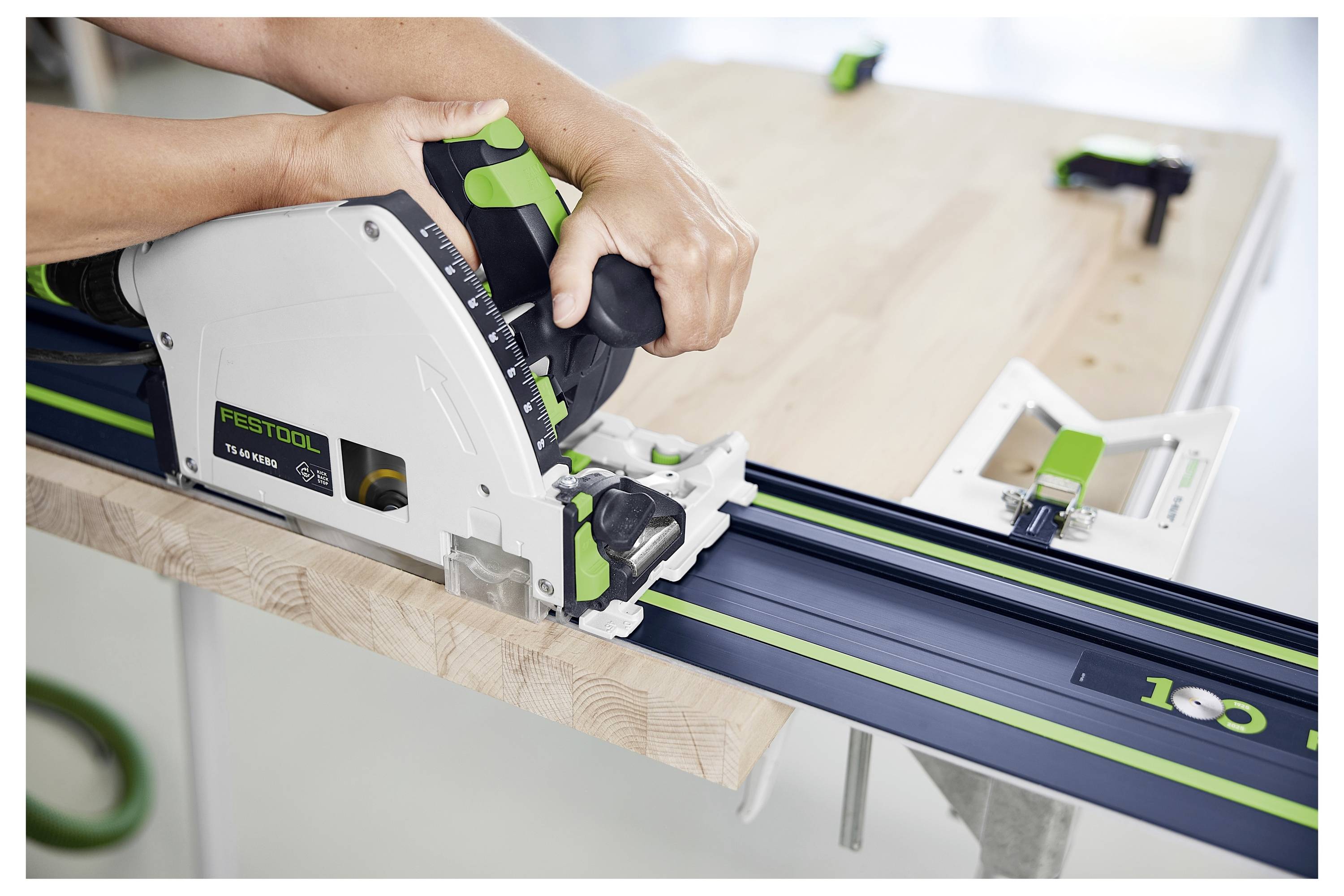 Une personne utilise une scie circulaire sur un rail de guidage pour effectuer une coupe précise sur une planche en bois dans un atelier.