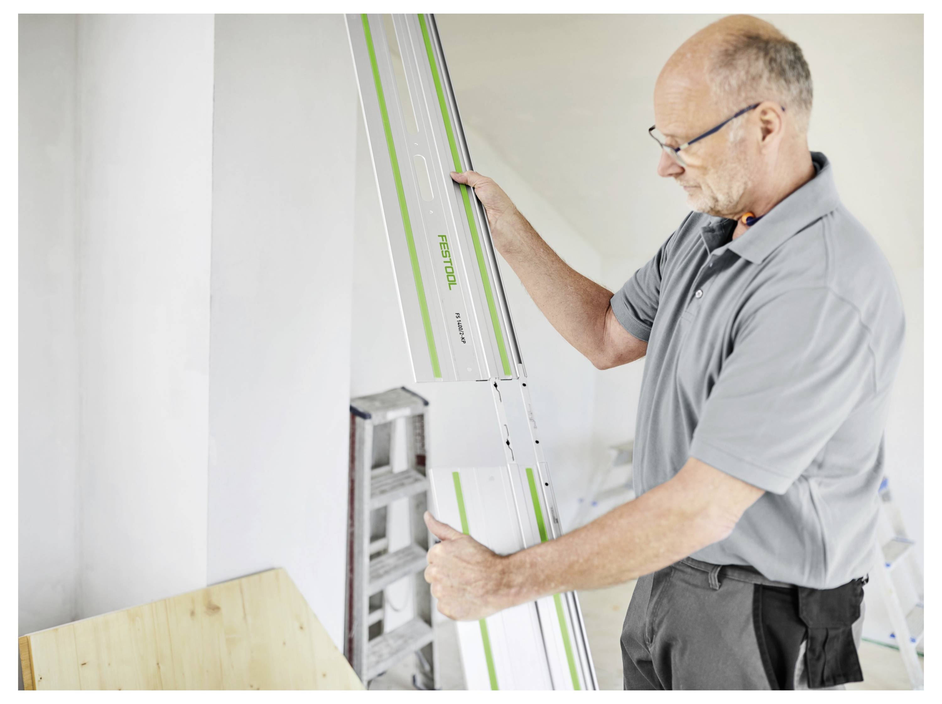 Une personne aligne un long outil de mesure rectangulaire sur un mur, semblant concentrée et prudente. Elle se trouve dans une pièce de couleur claire.