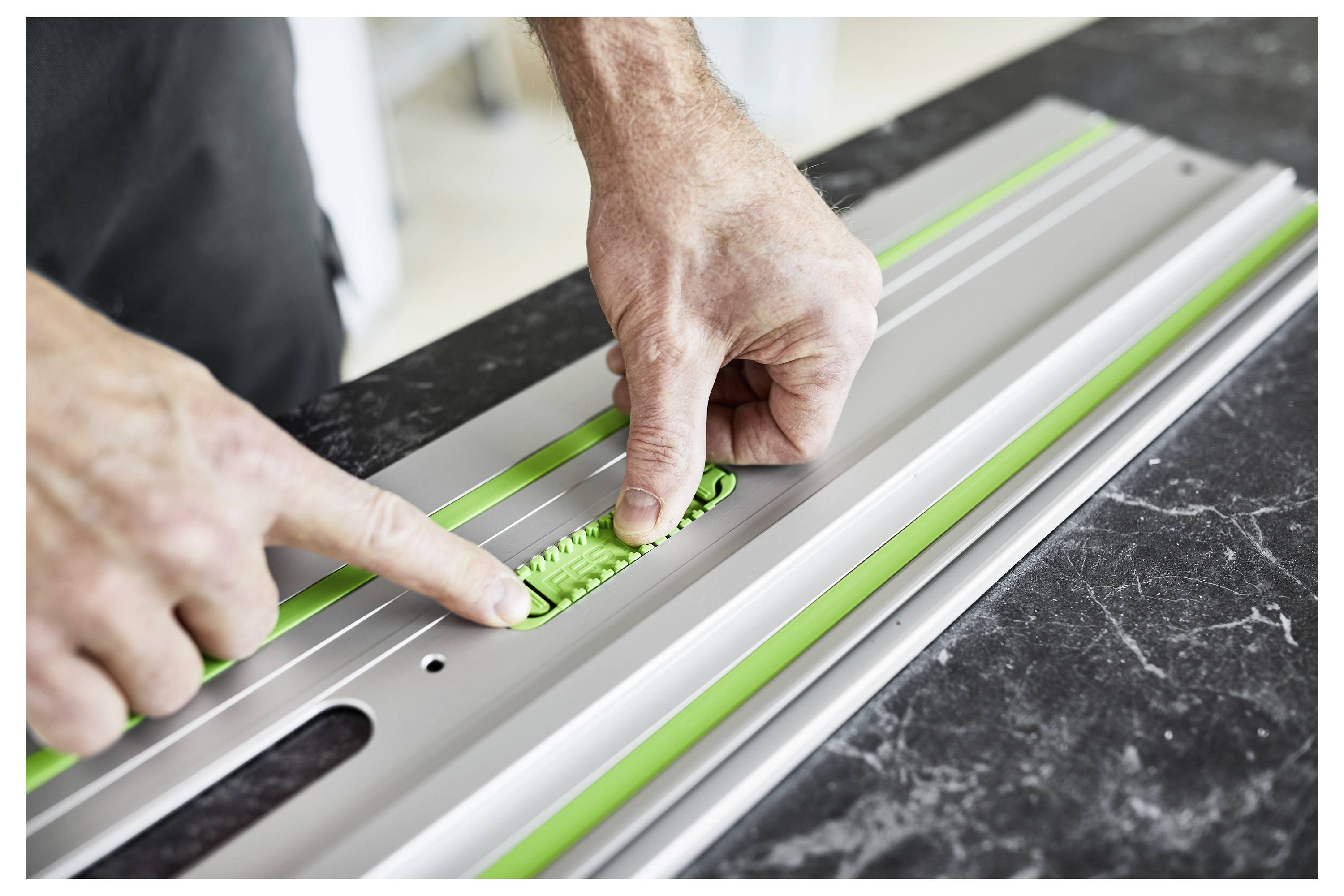 « Les mains ajustent un outil de mesure vert et argenté sur une table noire, se concentrant sur la précision et l'alignement dans un cadre d'atelier. »