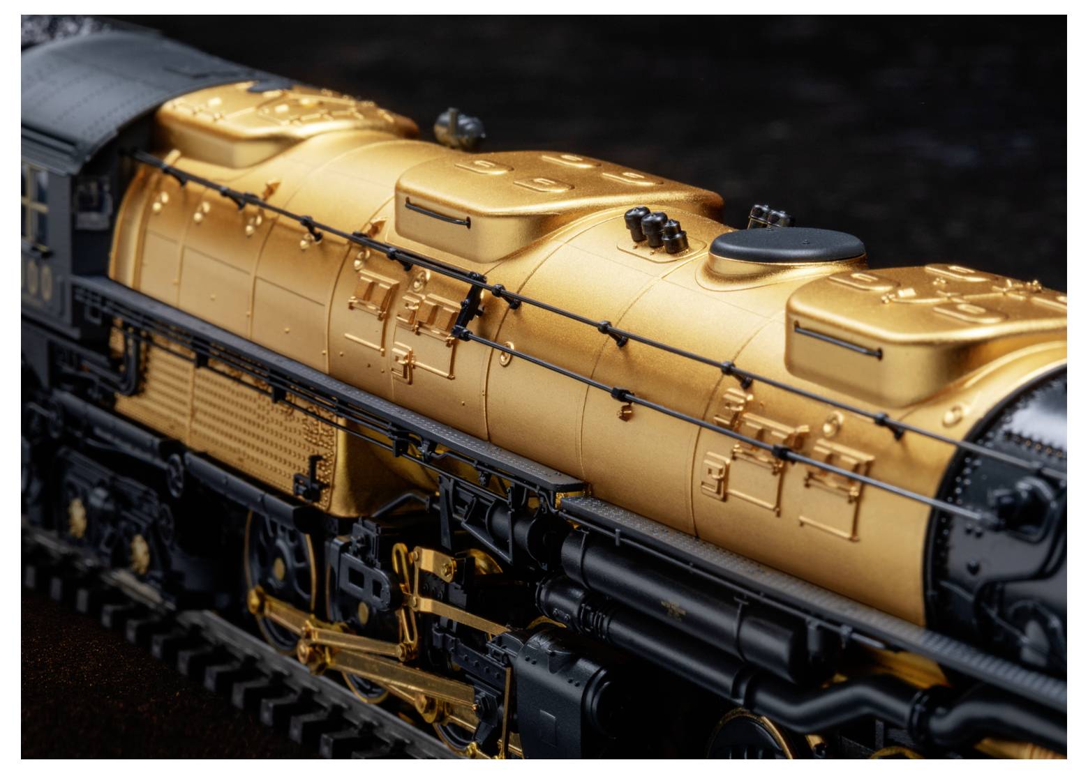 Un gros plan d'une locomotive de train miniature détaillée avec un schéma de couleurs orange et noir, montrant les composants mécaniques complexes et les textures.