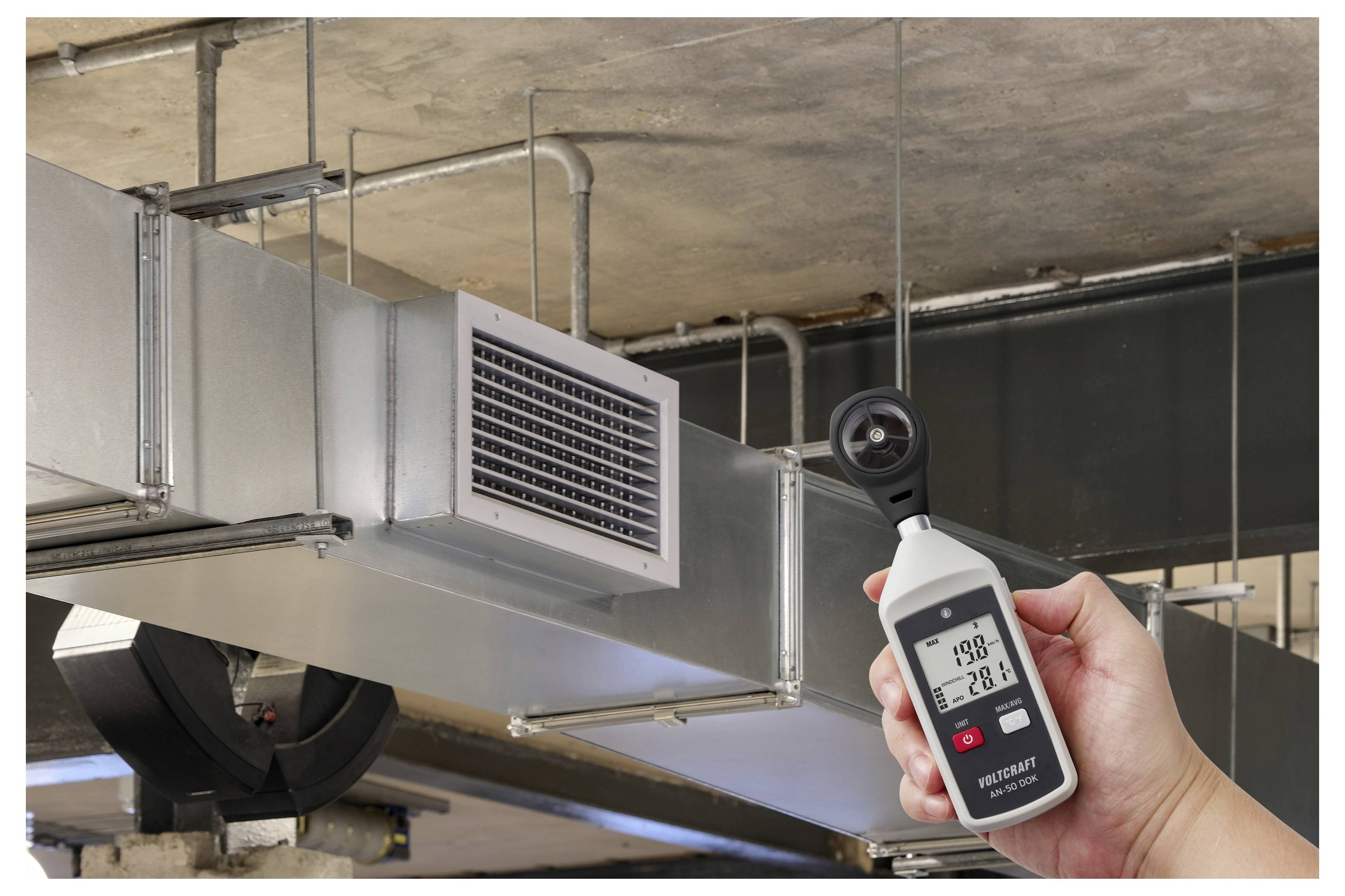 Débitmètre d'air portatif mesurant le flux d'air près d'un grand conduit de ventilation métallique dans un espace de plafond.