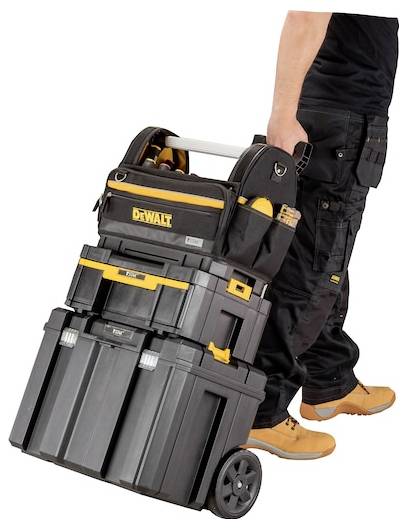 Une personne portant des bottes de travail et un pantalon noir tire une caisse à outils DeWalt empilable sur roulettes, appropriée pour transporter des outils et de l'équipement.