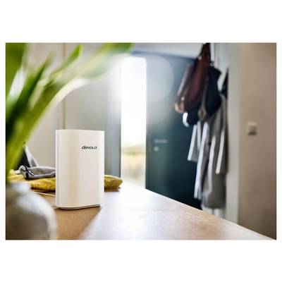 Un petit appareil électronique blanc portant l'inscription « devolo » est posé sur une table en bois dans une pièce lumineuse, avec un arrière-plan flou d'une porte.