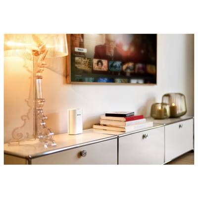 Un salon moderne avec une lampe allumée sur un meuble blanc, des livres empilés, des bougies et un téléviseur affichant divers choix multimédias.