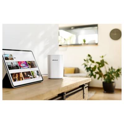 Une tablette sur une table affichant des vidéos à côté d'un appareil blanc étiqueté « devolo », dans un salon moderne décoré de plantes.