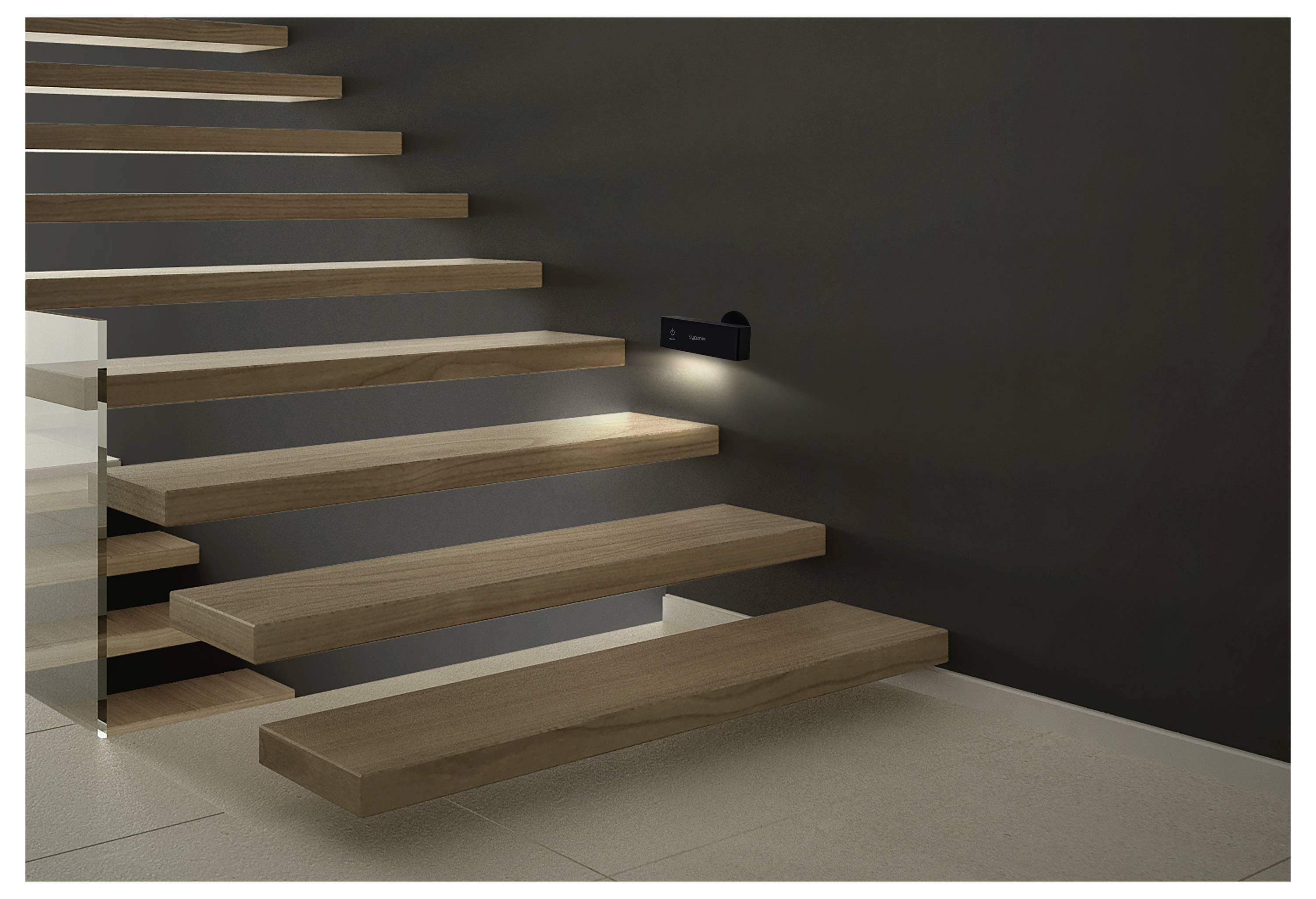 Escalier flottant en bois moderne contre un mur sombre, éclairé par une petite applique murale, avec des marches ouvertes et une rampe latérale en verre.