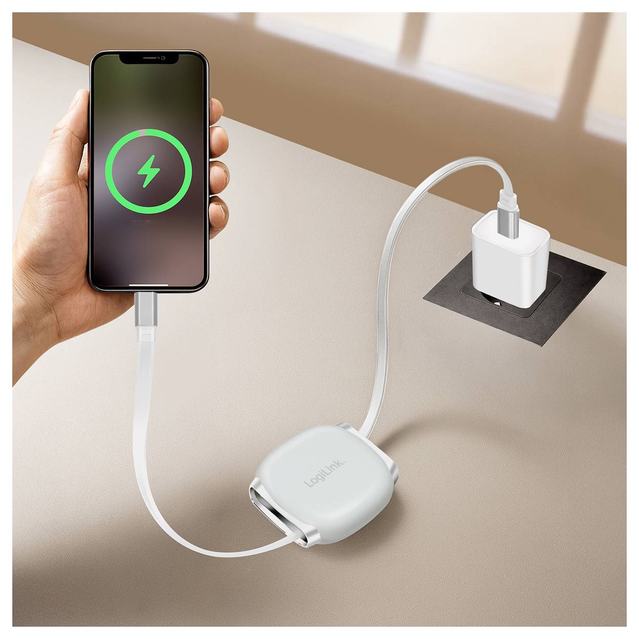 Une main tient un smartphone affichant un symbole de charge. Le téléphone est connecté à une prise murale via un câble de charge enroulé et un adaptateur.
