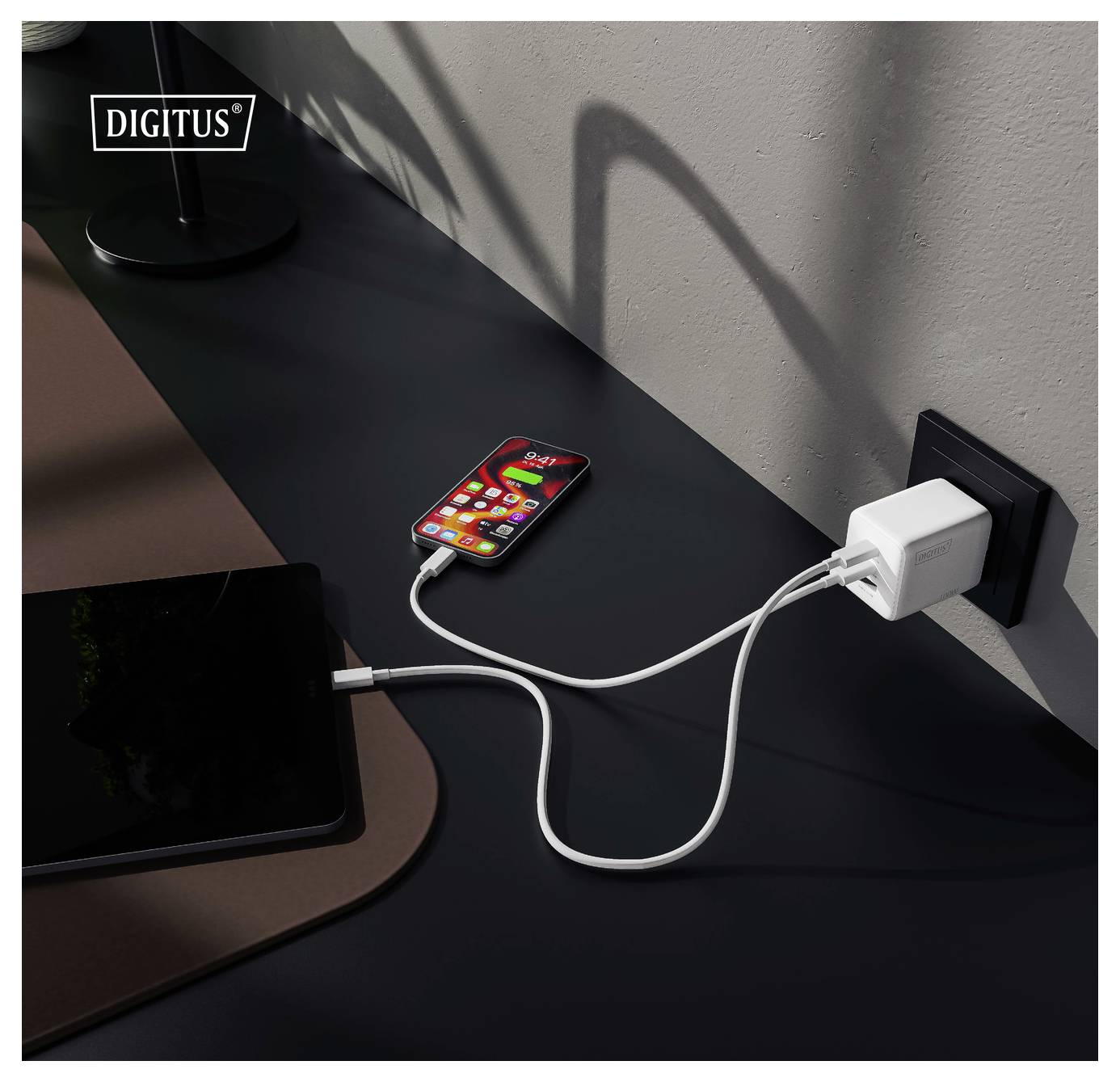 Un smartphone et une tablette se chargent sur un bureau à l'aide d'un chargeur mural à deux ports.