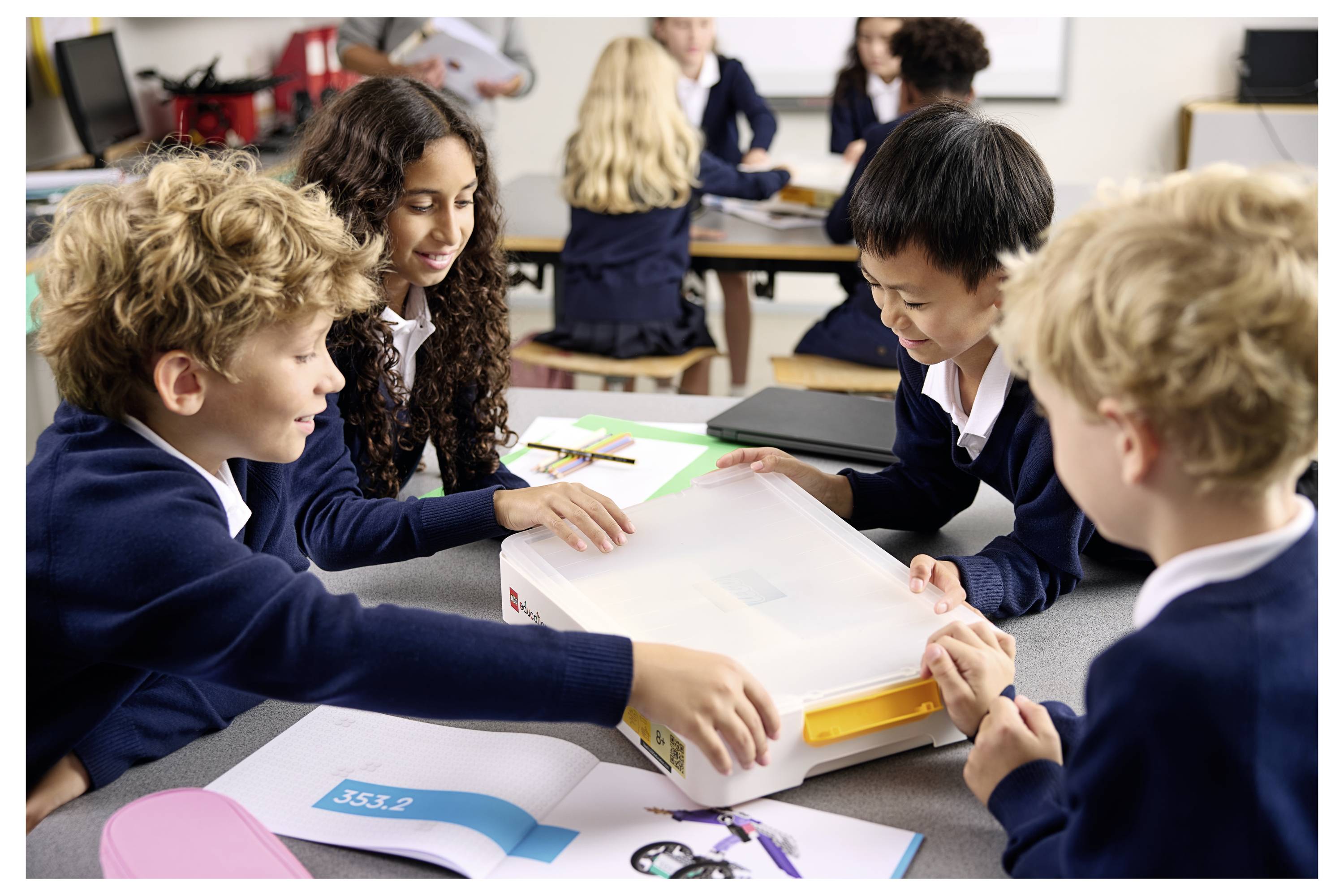 « Quatre enfants en uniformes scolaires travaillent ensemble sur un projet à une table de classe, avec des papiers et une boîte sur la table. »