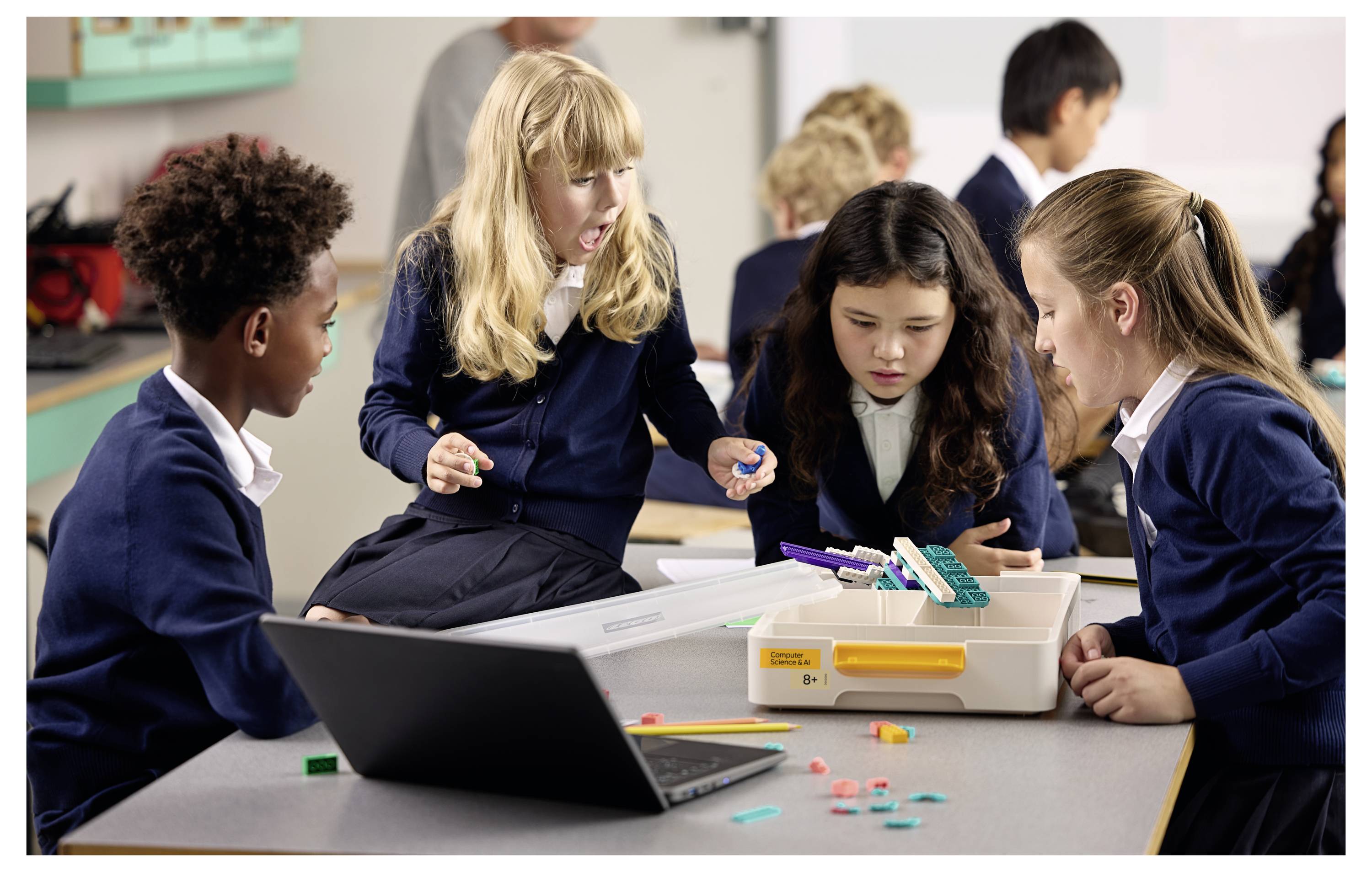 « Quatre étudiants en uniformes scolaires collaborent sur un projet STEM avec des blocs et un ordinateur portable dans un cadre de salle de classe. »