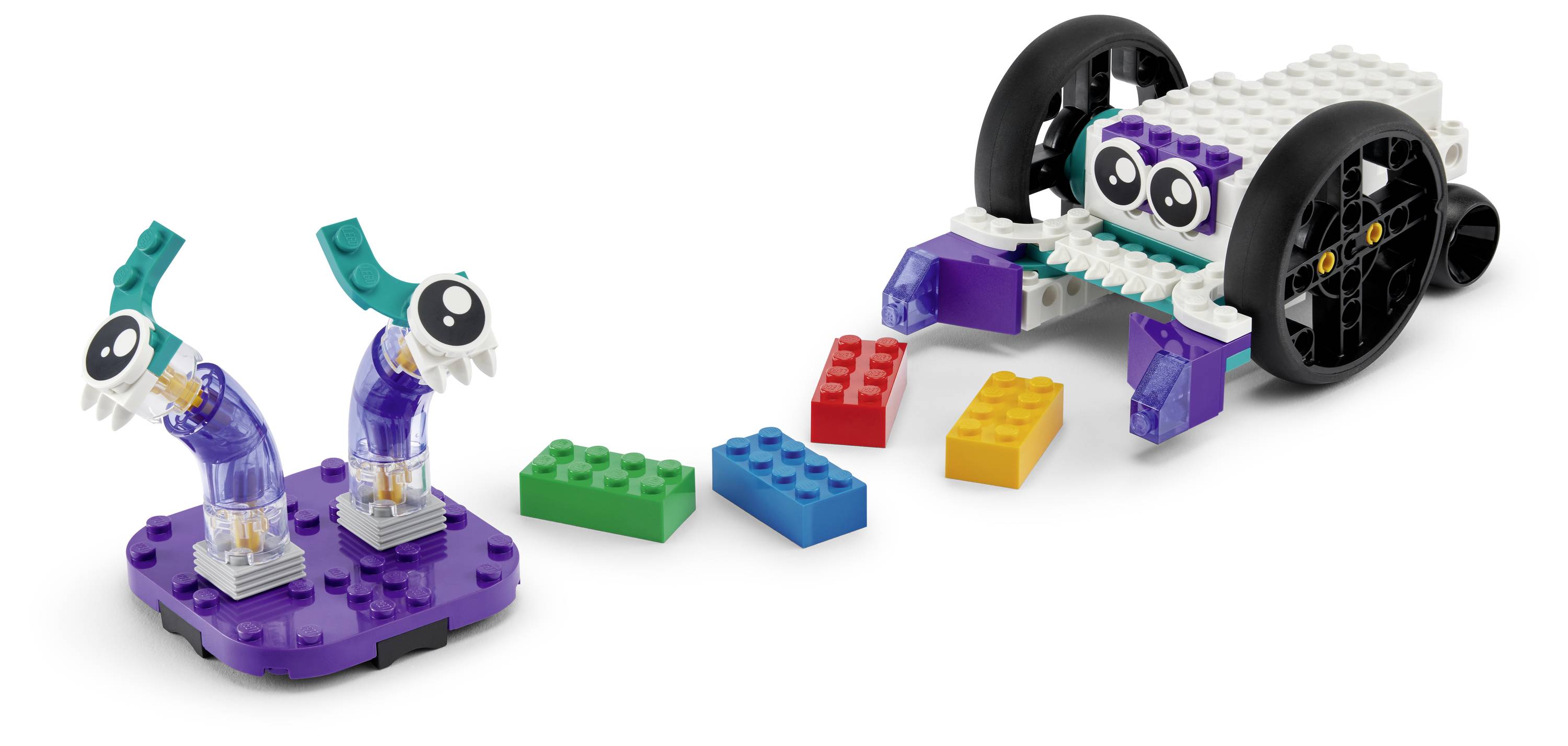 Un robot LEGO sur roues avec des autocollants en forme d'yeux fait face à deux autres structures LEGO, tous dans diverses couleurs, disposés sur un fond blanc.