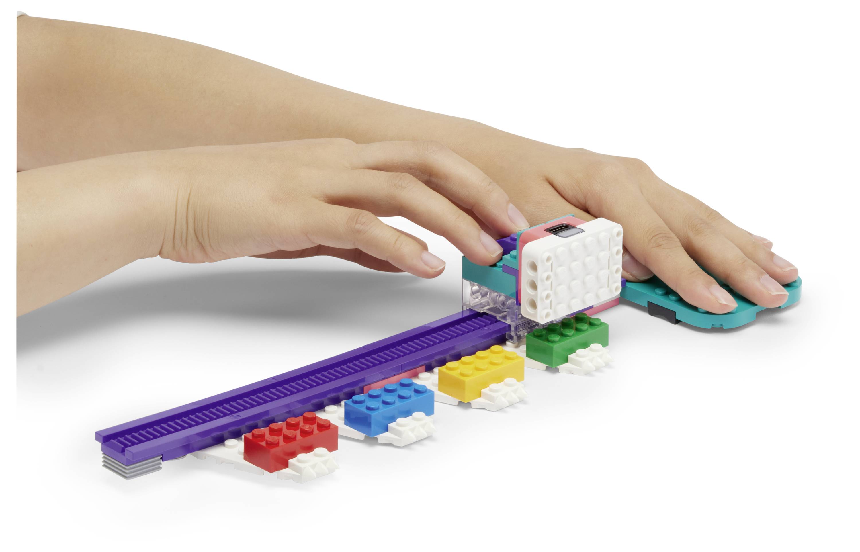 Deux mains utilisent des briques de jouet colorées avec une piste violette et un composant électronique, démontrant une tâche d'apprentissage ludique.